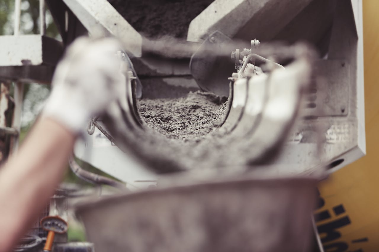 portfolio-02 Close-up of concrete being poured from a mixer truck at a construction site with a worker's hand visible.